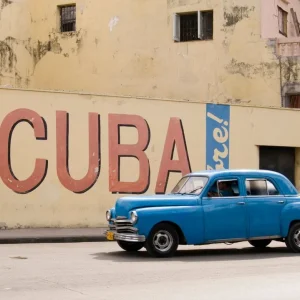 A vintage 1950s American car passing a Viva Cuba sign painted on a wall in cental Havana Cuba Satisfait Ou Remboursé