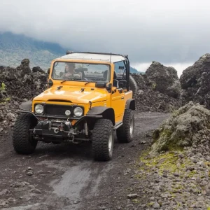 A curly-haired man is looking away driving an offroad yelow vehicle at the top of a valley with dark ground road Seulement Aujourd'hui